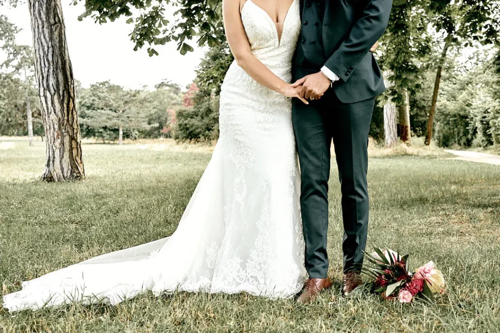 Photo d'un couple de mariés dans un parc. On peut voir l'entièreté de leur corps, sauf leurs têtes. Le bouquet de fleur est par terre à côté d'eux.