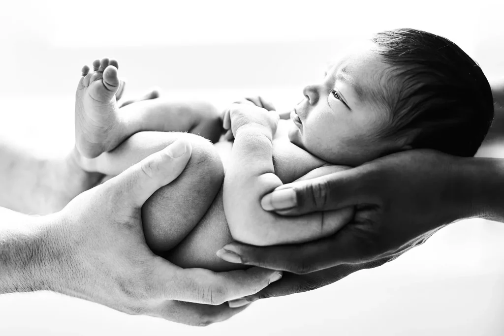 Portrait en noir et blanc d'un bébé enveloppé des mains de ses parents