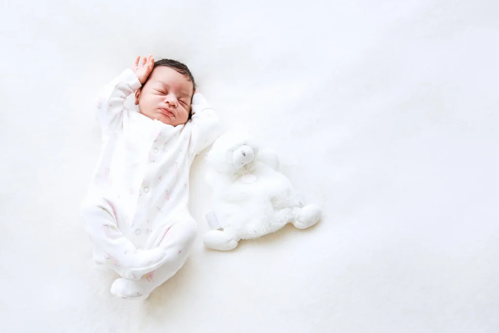 Photographie mignonne d'un nouveau-né à coté de son doudou sur fond blanc