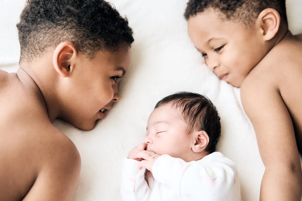 Photographie d'un bébé et ses deux grands frères allongés à côté de lui