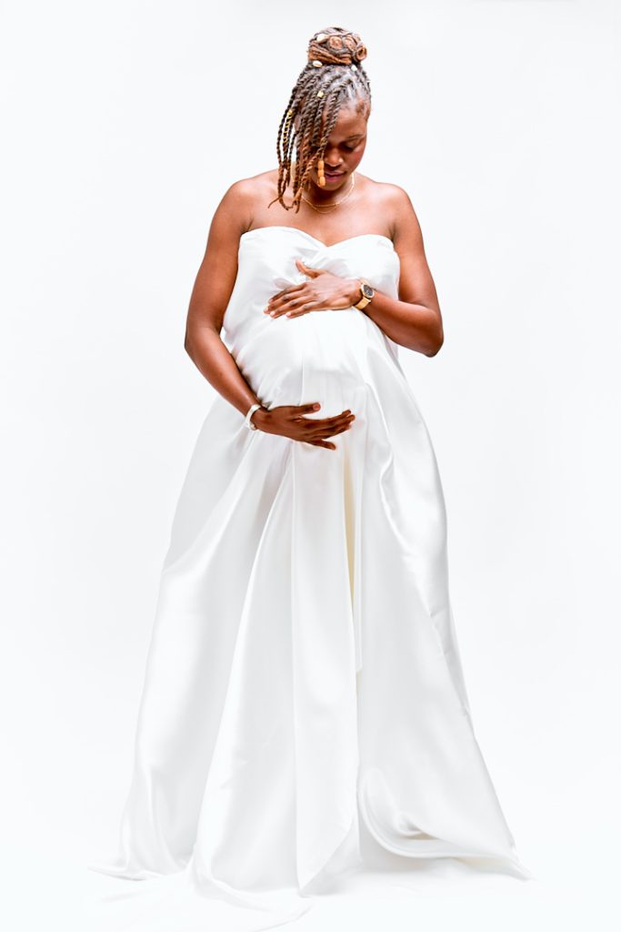 Portrait de femme enceinte debout avec un voile blanc, regardant vers son ventre