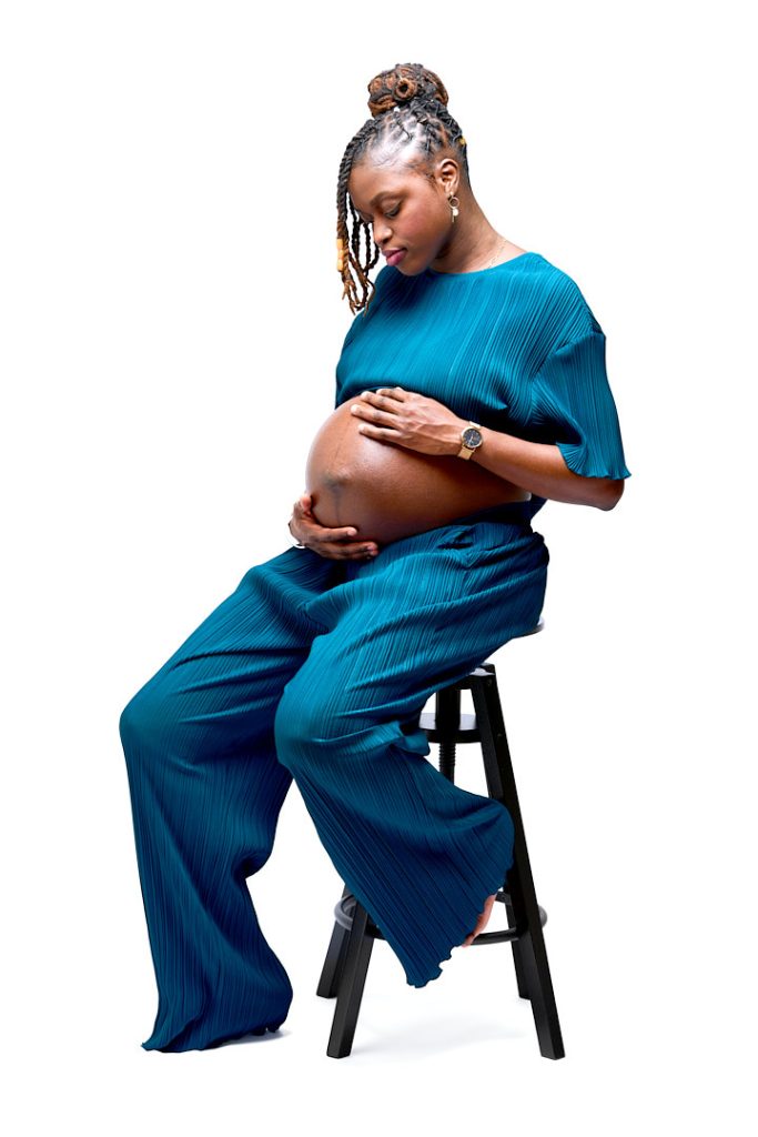 Portrait de femme enceinte noire, assise au studio avec un ensemble bleu vert