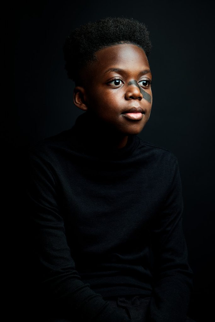 Portrait d'un jeune garçon noir qui regarde vers le côté. Fond noir et vêtements noirs.