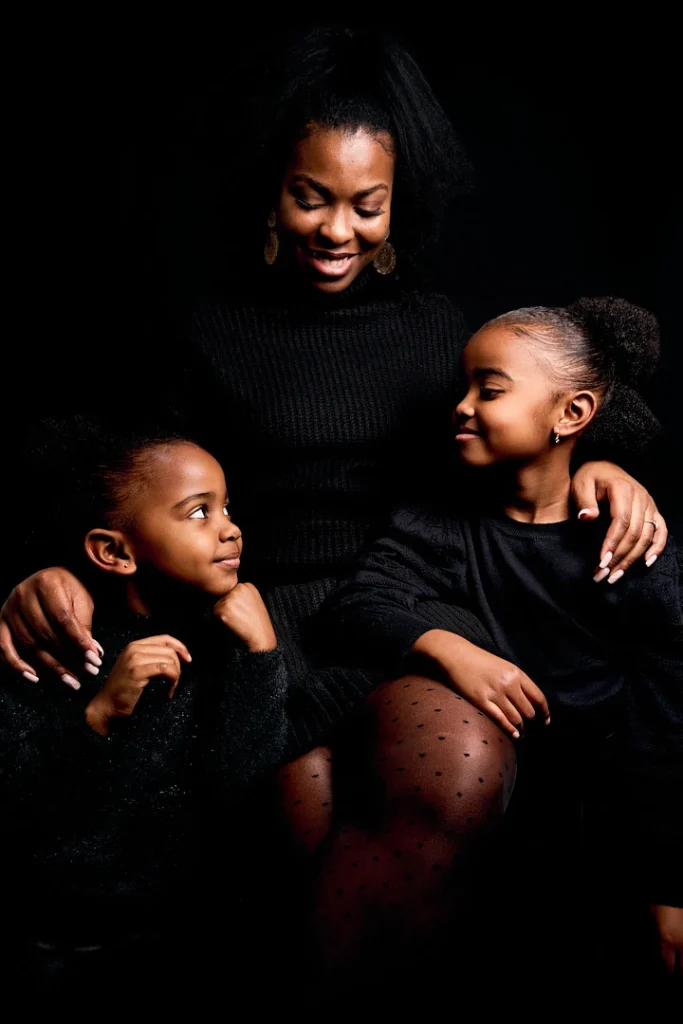 Photos de famille à la peau noire. La mère est assise et les filles sont debout à ses cotés (gauche et droite) et se regardent.