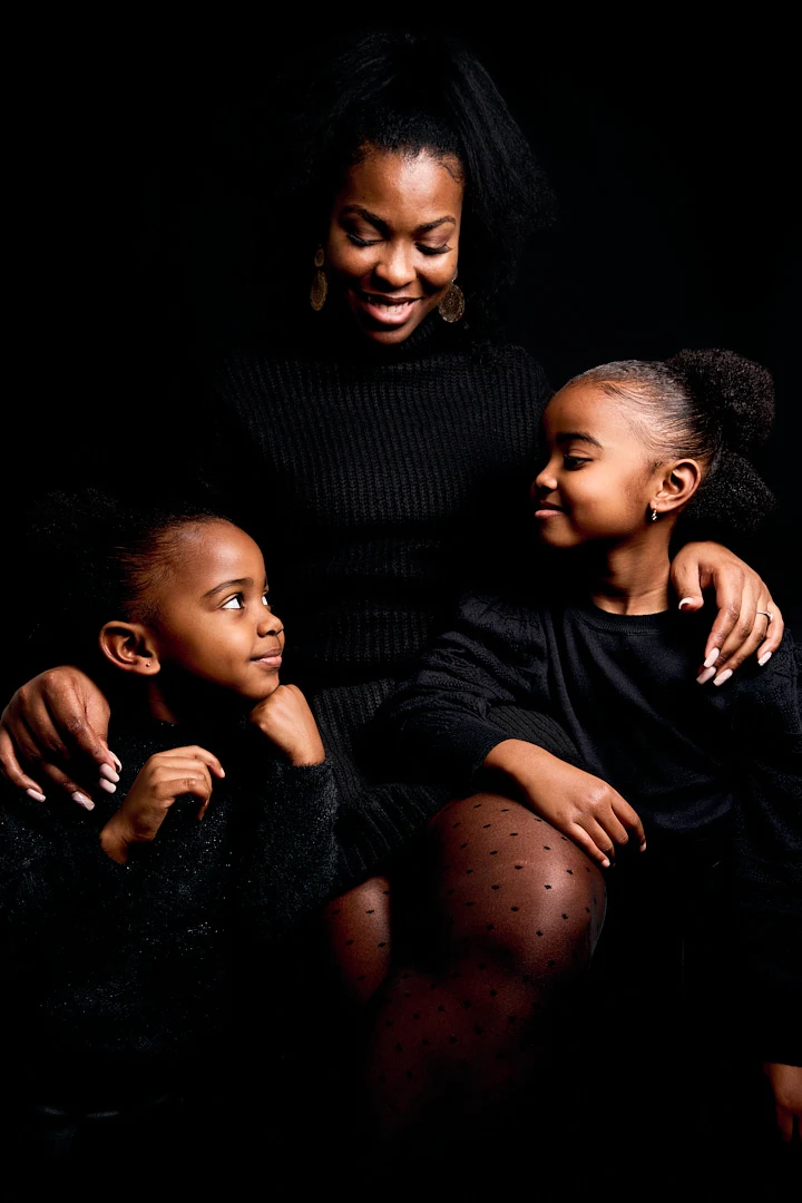 Photos de famille à la peau noire. La mère est assise et les filles sont debout à ses cotés (gauche et droite) et se regardent.
