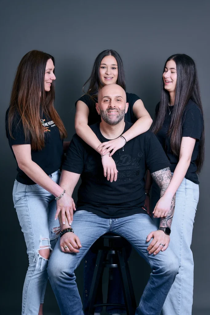 Portrait de famille blanche sur fond gris. Le père est assis, la mère et les deux adolescentes sont debout autour du père.