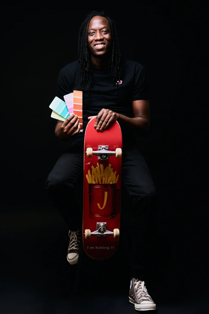 Portraits corporate d'un homme noir en studio avec un nuancier de couleurs dans les mains en référence à son métier de peintre et un skate en dessous en référence à sa passion, regardant vers l'objectif