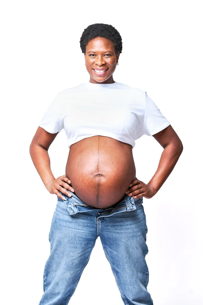Portrait de grossesse, femme noire regardant vers l'objectif avec le sourire et une position superman avec les mains sur les hanches